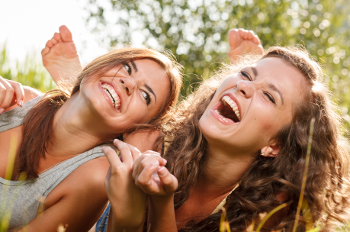 two girlfriends in T-shirts  lying down on grass laughing having good time